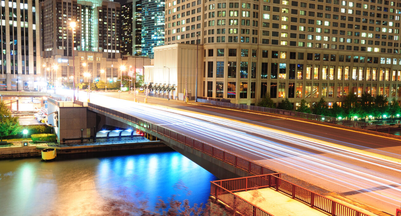 Chicago River Walk with urban skyscrapers and bridge illuminated with lights and water reflection at night.
