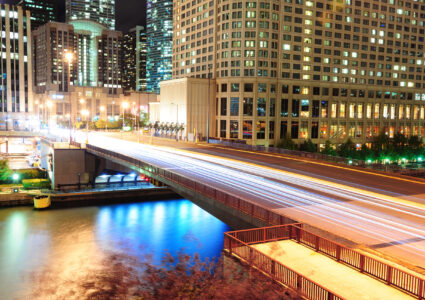 Chicago River Walk with urban skyscrapers and bridge illuminated with lights and water reflection at night.